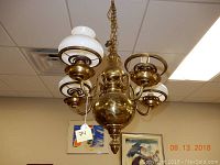 Front view of the antique brass chandelier showing the central brass body, four glass shades, and one missing glass shade.