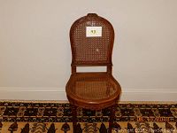 Front view of a vintage wooden cane chair with woven seat and backrest against a beige wall.
