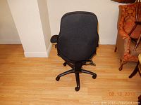 Rear view of black ergonomic office chair showing cushioned backrest and five-wheel base.
