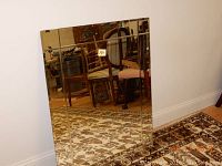 Rectangular beveled edge mirror leaning against wall on patterned carpet with furniture reflection visible.