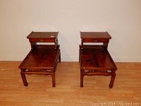 Pair of Mid Century night stands or end tables with Chinese motif carved aprons and elevated back shelves, reddish-brown finish.