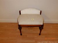 Front view of upholstered vanity chair with white fabric seat and back and carved wooden legs on hardwood floor