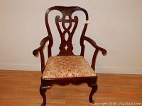 Single front view of antique-style wooden armchair showing carved backrest and upholstered seat.