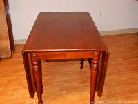 Front angle view of wooden drop leaf table showing one leaf down and one leaf up, with fluted turned legs visible.