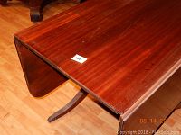 Photo showing a close-up of wooden drop leaf table top with one leaf raised, revealing the wood grain and rounded edges.