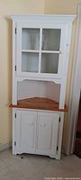 Full view of white corner hutch showing glass-panel door, open shelf, lower cabinet