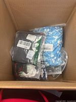 Top view of box showing blue floral garment and several black packaged garments