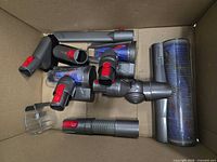 Box containing various Dyson quick-release accessories including floor head, mini motorized tool, wand section, hose, elbow joint
