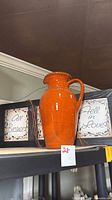 Wall plaque and orange terracotta pitcher on shelf