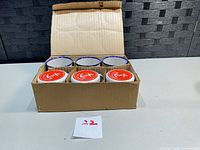 Box of six enamel mugs, three bases up showing red logo, three open tops showing blue rims