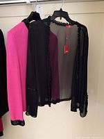 Pink cardigan and black sheer blouse on hangers