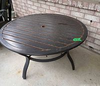 Side view of bronze metal round patio table showing legs, slatted top, umbrella hole, surface rust