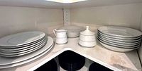 Stacks of plates, bowls, creamer, lidded sugar on shelf