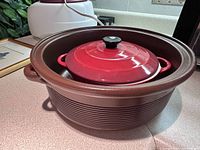 Brown stoneware Dutch oven holding red pot