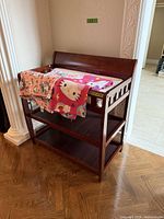 Full view of dark cherry changing table with pad and blankets on top