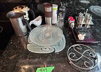 Countertop view showing stacked glass plates, moka pot, pitcher, spice set, trivet and other small items