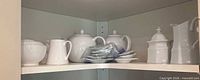 Shelf with sugar bowl, creamer, teapot, stack of small plates, second teapot, lidded jar, tall pitcher
