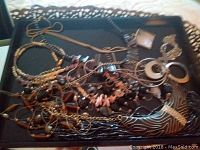 Various costume jewelry including beaded bracelets and necklaces, crosses, and large circular metallic earrings placed on a black mirrored tray with ornate edges and patterns.