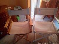 Both folding directors chairs side by side showing natural wood and white frames with beige canvas seating and backs
