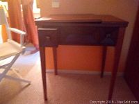 Full view of vintage sewing machine wood table showing front and side with legs, drawer and hinged top.