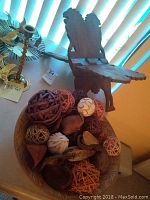 Wood bowl containing various decorative natural items such as woven rattan balls and dried pods, with carved wooden book stand in the background.