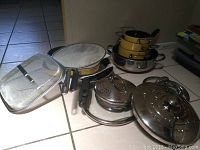 Assorted yellow saucepans, frying pans, stainless steel mixing bowls and various mesh lids and covers