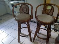 Two vintage caneback stools with woven backs and beige upholstered round seats shown together in a kitchen setting on a tiled floor.