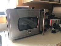 Front view of the Kitchentek Pressure Oven showing stainless steel construction with glass door and metal handle, and dials for controls on the side.
