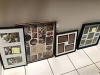 Four photo frames arranged on floor against wall: multi-photo black and white matted frames and brown plastic collage frame