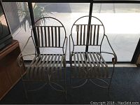 Two off-white metal outdoor chairs next to a window, showing their front, seat, and back designs.