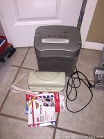 Photo showing the Royal shredder, Design Concepts laminator, and opened package of 3M laminating pouches on a tiled floor near a door.