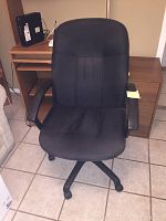 Front view of the black cloth office chair showing cushioned seat, backrest, armrests, and caster wheels.