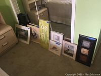Photo showing assortment of framed paintings and needlepoint artwork, various sizes and styles including vertical tulip painting and seashell paintings
