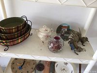 Photo showing two brass rooster figurines, ceramic soup bowl, decorative Irish plate, and potpourri bowl on a white shelf.