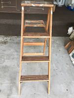 Front view of wooden ladder showing four foot height and three stepped rungs with wood grain visible.