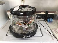 Clear image of Nuwave Pro Infrared Oven on stove with black top and glass cooking bowl, including metal racks inside and recipe manual