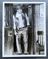 Front view of NBC 7x9 photo showing John Wayne holding rifle in doorway