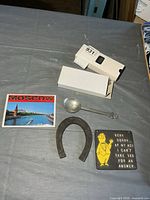 Group shot showing all six items: Moscow photo booklet, two pen/magnifier cases, metal spoon, rubber horseshoe, aluminum plaque