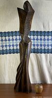 Full view of tall carved wood abstract figure on tabletop with apple for scale