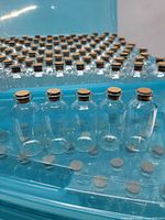 Close-up of front row of clear glass vials with corks in blue tray