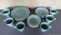 Complete dinnerware set arranged on table: dinner plates, salad plates, bowls, mugs