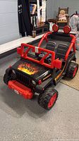 Full view of black and red Power Wheels Jeep Wrangler style ride-on with flame hood decal, dual seats, roll bar and wheels