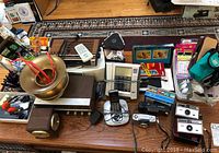 Wide shot of lot showing Zenith radios, Panasonic cordless phone, Kodak Instamatic cameras, Olympus Pen and Canon Snappy cameras, pens and cuspidor