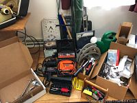 Photo showing clock, power drill, air compressor, garden stakes, and boxed items on floor next to a table