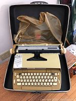 Front view of the beige and brown Smith Corona Automatic 12 typewriter in an open case with plastic dust cover.