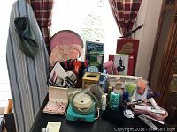Full view of table with Rival steam iron, Lady Sunbeam electric shaver box, travel kit, personal care items, and ironing board in background