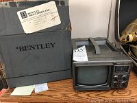 Front view of Bentley portable TV model 100C with original box behind it on wooden surface.