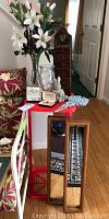 Wide view of the lot showing two framed mirrors, red plastic stand, trinket case, jewelry, vases, and sculpture arranged on floor and table.