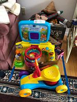 V-Tech Smart Shots Sports Center with basketball hoop and Playskool ride-on toy in front of a couch with stuffed animals and Scrabble game box behind.