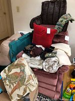 Chair with assorted linens, red cushion, gloves, and bird tapestry cushion visible.